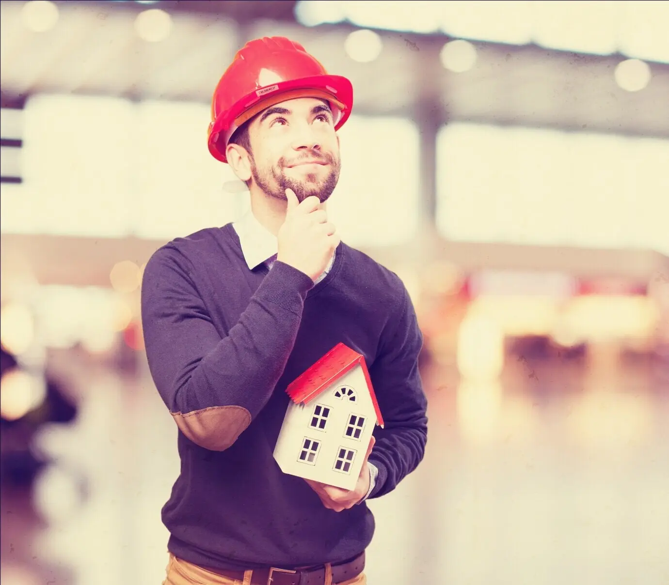 A man with a red helmet holding a small house in his hand.